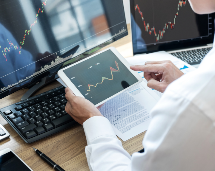 A man looks at financial information on multiple screens, a desktop, laptop and tablet